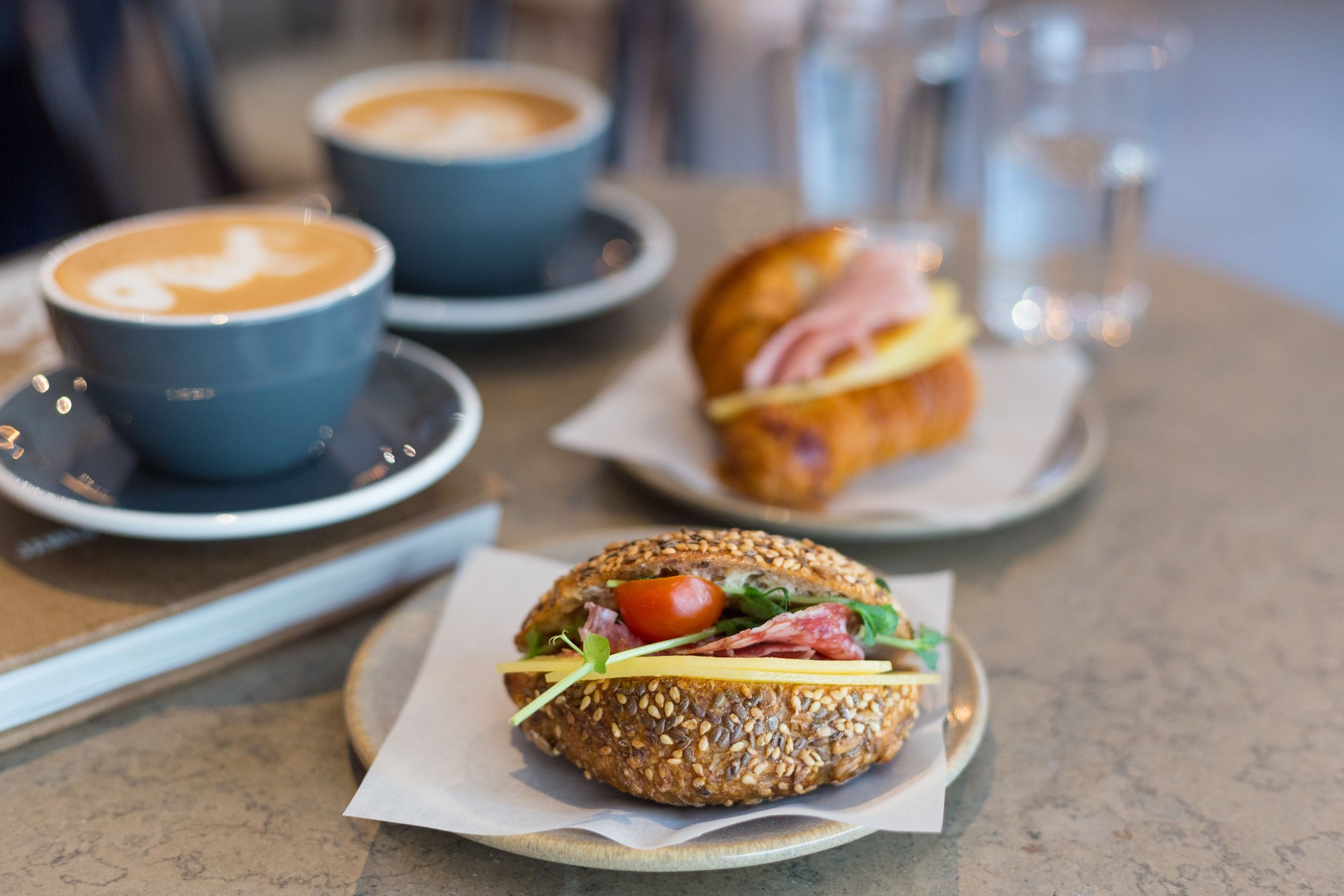 Two cups of cappuccino with latte art, sandwich and croissant on marble background. Concept of easy breakfast. Gray ceramic cups